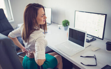 Young woman having back pain while sitting at desk in office HOME OFFICE